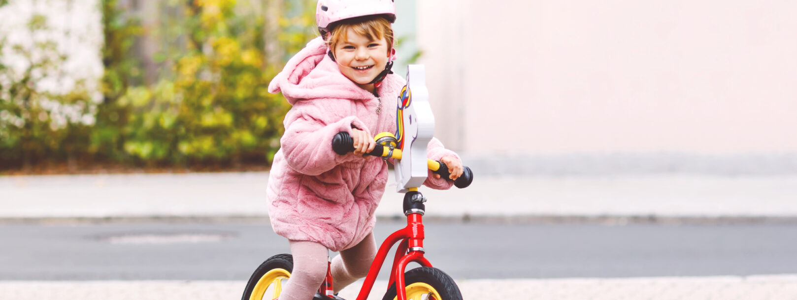 Lille smilende pige med cykelhjelm der leger med sin loebecykel