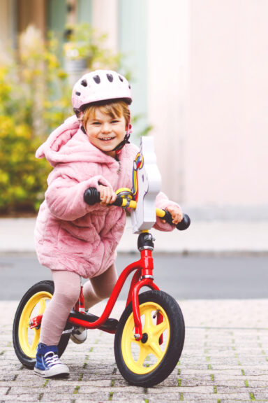 Lille smilende pige med cykelhjelm der leger med sin loebecykel